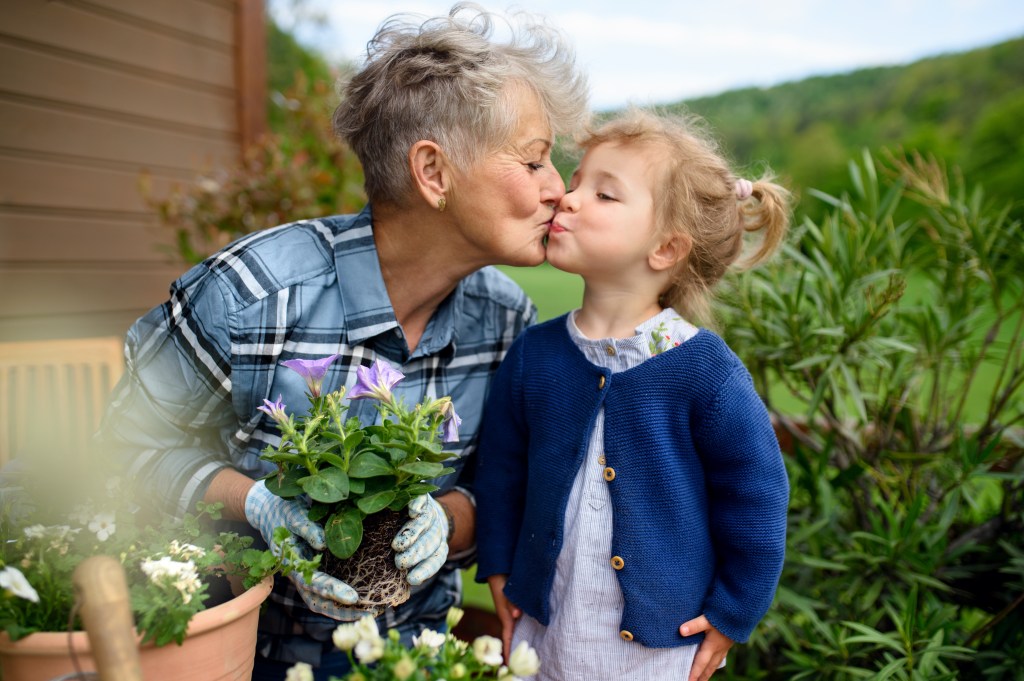 Happy elderly grandmother with little granddaughter blooming on balcony in summer, kissing.